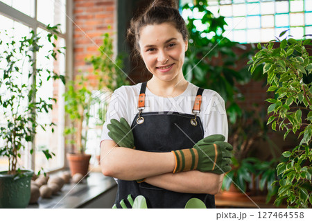 Running of own business. Young woman florist wearing apron in botanical store with green plants. Happy small business owner working at flower shop standing surrounded by plants. Small business 127464558