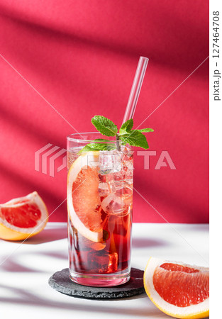 Refreshing cocktail with grapefruit, mint and ice in a glass on a white red background with shadow Refreshing cocktail with grapefruit, mint and ice in a glass on a white red background with shadow 127464708