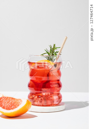 Refreshing mocktail with grapefruit, rosemary and ice in a glass on a light background with shadows. Refreshing mocktail with grapefruit, rosemary and ice in a glass on a light background with shadows. 127464714