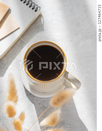Freshly brewed espresso coffee in mug on a light table illuminated by the sun, with notebooks Freshly brewed espresso coffee in mug on a light table illuminated by the sun, with notebooks 127464715