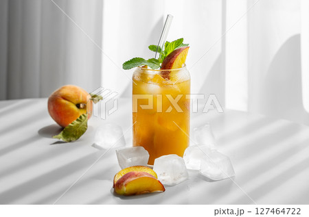 Refreshing peach cocktail, lemonade or iced tea on a white table near window with shadows  127464722