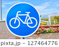 A blue and white traffic sign displaying a bicycle symbol against a backdrop of the sky and clouds. The image includes a bicycle wheel, tire, frame, and a plant in the background 127464776