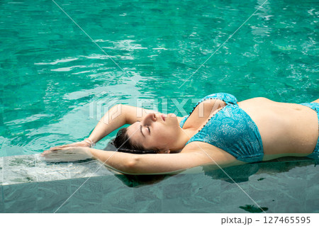 Young woman lying in swimming pool with turquoise water and opened arms in zen gesture Young woman lying in swimming pool with turquoise water and opened arms in zen gesture 127465595