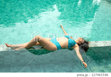Top view of young model lying in swimming pool with turquoise water and opened arms Top view of young model lying in swimming pool with turquoise water and opened arms 127465596