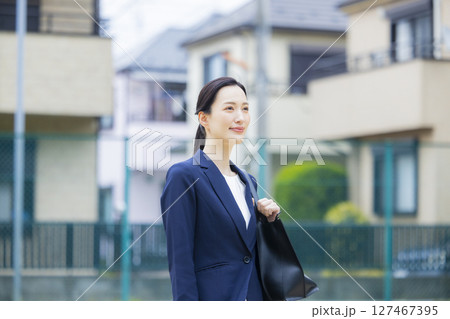 住宅街を歩くスーツを着た若い女性 127467395