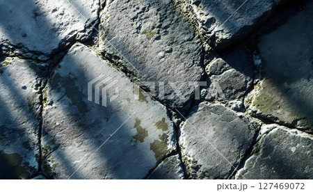 A textured stone wall casting intricate shadows, creating a play of light and dark across its surface 127469072