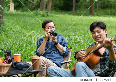 Family fun captured. Father photographing son playing guitar outdoors. 127470511