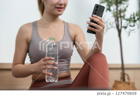 Hydration and fitness. Young woman holding a water bottle while checking her smartphone. 127470609
