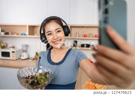 ESG and Healthy Lifestyle. Young woman enjoying a salad while taking a selfie in a modern kitchen. ESG and Healthy Lifestyle. Young woman enjoying a salad while taking a selfie in a modern kitchen. 127470623