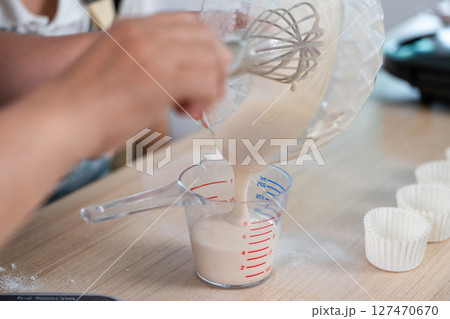 Family Cooking Fun. A child pouring batter into a measuring cup with mom's guidance. 127470670