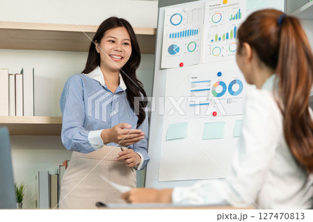 Engaging Business Presentation. Female professional explaining data insights to colleague in office. Engaging Business Presentation. Female professional explaining data insights to colleague in office. 127470813