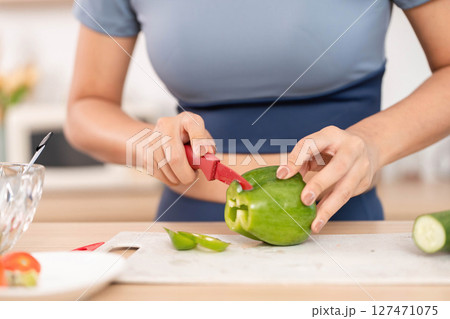 ESG and Vegetable Cutting. Woman slicing a green bell pepper in a modern kitchen. ESG and Vegetable Cutting. Woman slicing a green bell pepper in a modern kitchen. 127471075