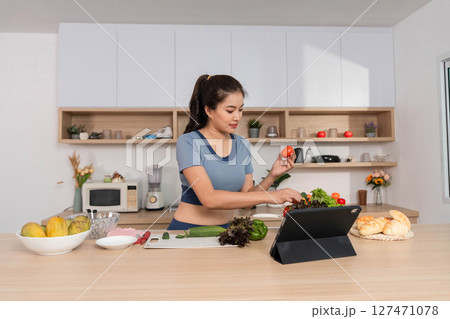 ESG and Cooking. Woman preparing a healthy meal while using a tablet in a modern kitchen. 127471078