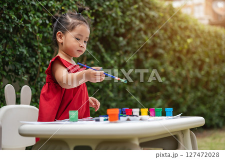 happy toddler girl painting watercolor in paper at backyard. 127472028