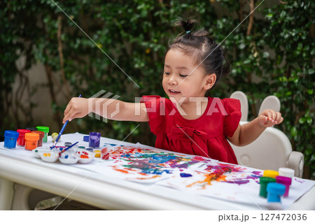 happy toddler girl painting watercolor in paper at backyard. happy toddler girl painting watercolor in paper at backyard. 127472036