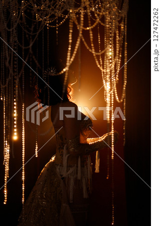 Young woman in vintage corset costume posing under chandelier on dark background Young woman in vintage corset costume posing under chandelier on dark background 127472262