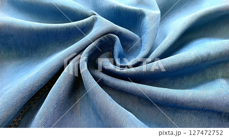 A close-up view of soft, blue fabric swirling into a spiral pattern, showcasing its smooth texture and vibrant color 127472752