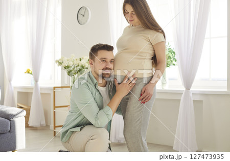 Future parents anticipating baby birth. Caring husband listening to child in mothers belly Future parents anticipating baby birth. Caring husband listening to child in mothers belly 127473935