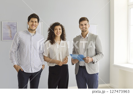 Young happy couple looking at camera in new house with man realtor. Real estate market concept. 127473963