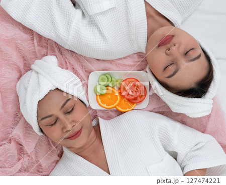 Two women enjoy a peaceful moment in a spa setting, dressed in white robes and towel. Fresh fruit is served nearby, enhancing the tranquil atmosphere. Two women enjoy a peaceful moment in a spa setting, dressed in white robes and towel. Fresh fruit is served nearby, enhancing the tranquil atmosphere. 127474221