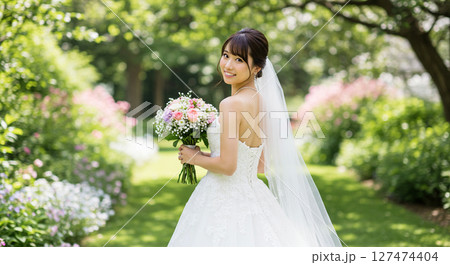 ガーデンウェディングでブーケを持ち、後ろに振り向く白いウェディングドレスを着た花嫁の姿 127474404