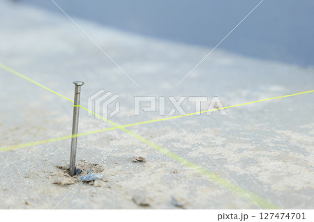 A close-up of a nail driven into rough concrete with intersecting yellow lines, representing detailed construction work for house tiling projects. 127474701