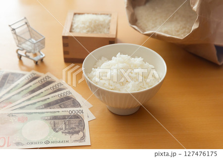 茶碗に盛ったごはん、1万円札、枡に入ったお米、米袋、ショッピングカート。米価のイメージ 127476175