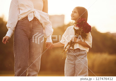 Kid is holding red flowers. Woman with her little daughter are on the summer field together 127476412