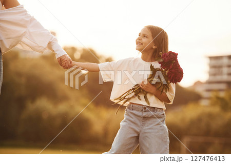 Kid is holding red flowers. Woman with her little daughter are on the summer field together 127476413