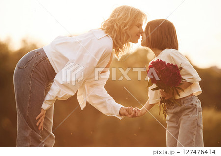 Kid is holding red flowers. Woman with her little daughter are on the summer field together 127476414