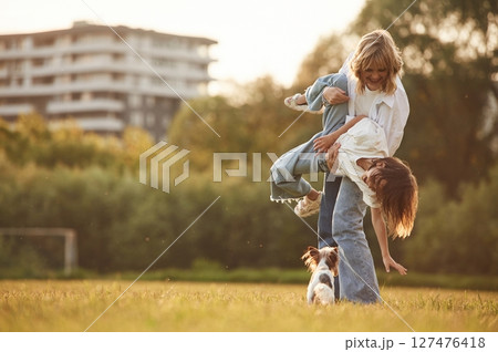 Holding kid in hands. Beautiful mother with her little daughter and dog are on the summer field together Holding kid in hands. Beautiful mother with her little daughter and dog are on the summer field together 127476418