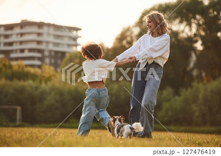 Beautiful mother with her little daughter and dog are on the summer field together Beautiful mother with her little daughter and dog are on the summer field together 127476419