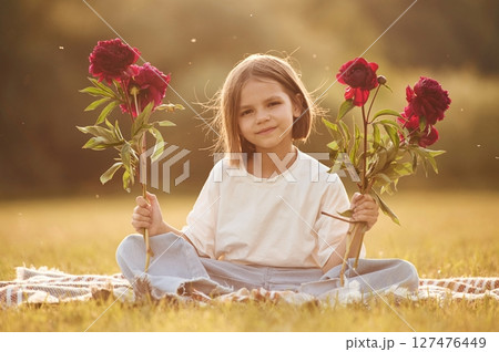 Red flowers in hands. Little girl is on the summer field at daytime 127476449
