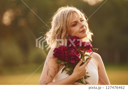 Portrait of beautiful young woman that is standing outdoors and holding red flowers 127476462
