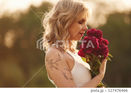 Side view. Beautiful young woman is standing outdoors and holding red flowers Side view. Beautiful young woman is standing outdoors and holding red flowers 127476466