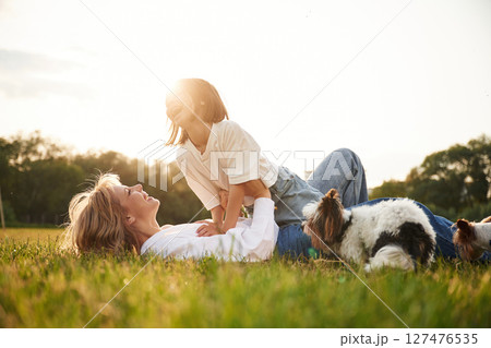 Laying down on ground. Beautiful mother with her little daughter and dogs are on the summer field together Laying down on ground. Beautiful mother with her little daughter and dogs are on the summer field together 127476535