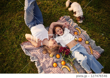 On the blanket with oranges and bananas. Woman with her little daughter are on the summer field together On the blanket with oranges and bananas. Woman with her little daughter are on the summer field together 127476546