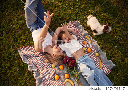 On the blanket with oranges and bananas. Woman with her little daughter are on the summer field together On the blanket with oranges and bananas. Woman with her little daughter are on the summer field together 127476547