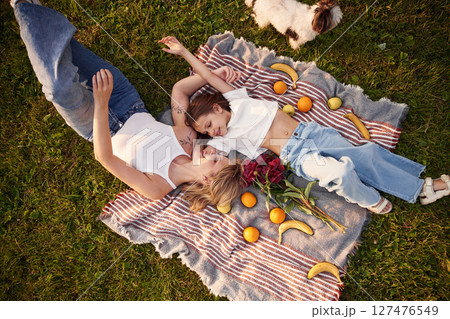 On the blanket with oranges and bananas. Woman with her little daughter are on the summer field together 127476549