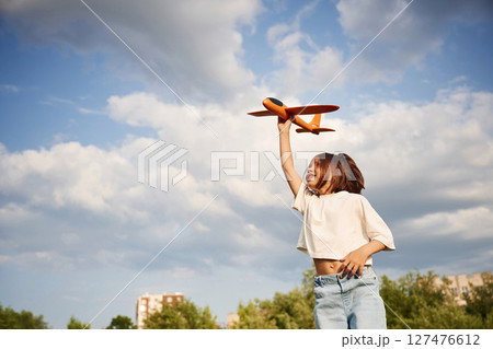 Cloudy sky. Happy little girl is playing with toy plane outdoors 127476612