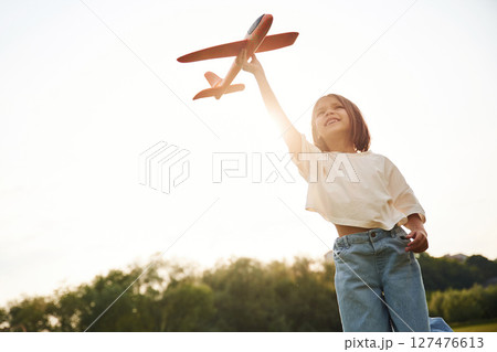 Front view. Happy little girl is playing with toy plane outdoors 127476613