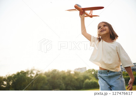Front view. Happy little girl is playing with toy plane outdoors Front view. Happy little girl is playing with toy plane outdoors 127476617