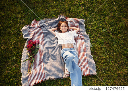 Top view. Laying down on the blanket. Flowers on the side. Little girl is on the summer field at daytime Top view. Laying down on the blanket. Flowers on the side. Little girl is on the summer field at daytime 127476625