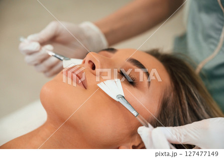 Cleaning skin by brushes. Woman face getting facial care by beautician hands at spa salon 127477149