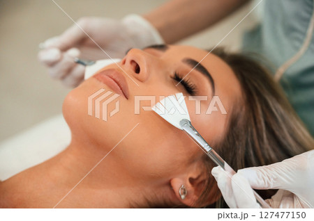 Cleaning skin by brushes. Woman face getting facial care by beautician hands at spa salon 127477150