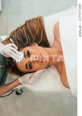 Woman face getting facial care by beautician hands at spa salon Woman face getting facial care by beautician hands at spa salon 127477169
