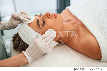 Woman face getting facial care by beautician hands at spa salon Woman face getting facial care by beautician hands at spa salon 127477170