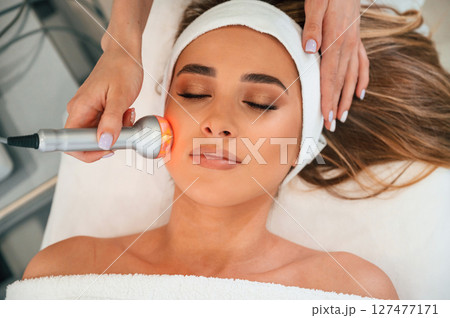 Apparatus for galvanization is used. Woman face getting facial care by beautician hands at spa salon Apparatus for galvanization is used. Woman face getting facial care by beautician hands at spa salon 127477171