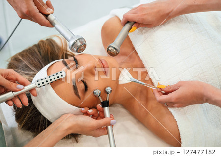 Hands are holding bunch of cosmetitian tools. Woman face getting facial care by beautician hands at spa salon Hands are holding bunch of cosmetitian tools. Woman face getting facial care by beautician hands at spa salon 127477182