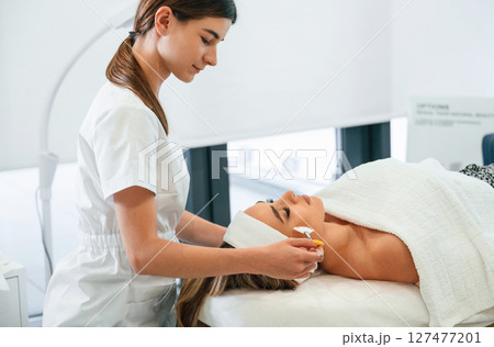 Side view. Woman face getting facial care by beautician hands at spa salon 127477201